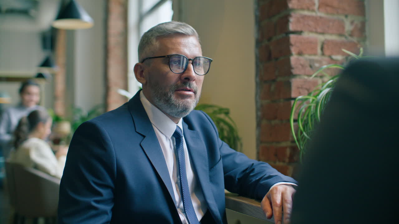 Senior Businessman Smiling and Talking with Colleague in Cafe