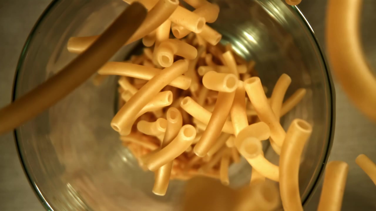 Maccheroni secchi che cadono in una ciotola di vetro al rallentatore