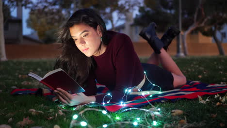 una joven atractiva leyendo un libro de cuentos o una novela en un parque al atardecer con luces brillando alrededor de su diapositiva izquierda