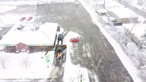 Maquinaria-Pesada-Limpiando-El-Estacionamiento-De-La-Nieve-Durante-Una-Tormenta-De-Nieve-Extrema,-Vista-Aérea