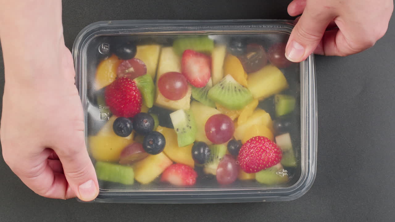 Hand Adding Blueberries to Fresh Mixed Fruit Salad