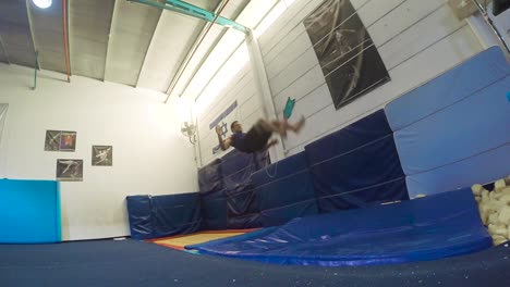 una toma en cámara lenta de un tipo haciendo volteretas desde el aterrizaje del trampolín y ganando divirtiéndose y haciendo ejercicio a 60 fps
