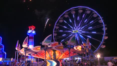 fireworks explode in the night sky behind a ferris wheel at a carnival or state fair