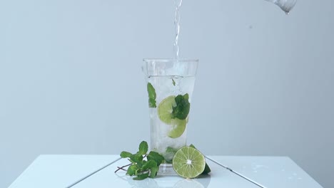 water-pours-into-glass-with-mint-and-lime-slices-inside