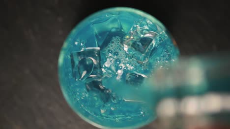 preparing a blue cocktail with soda and ice cubes, a hand puts ice cubes in the glass