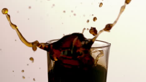 un cubo de hielo cayendo en un vaso de refresco