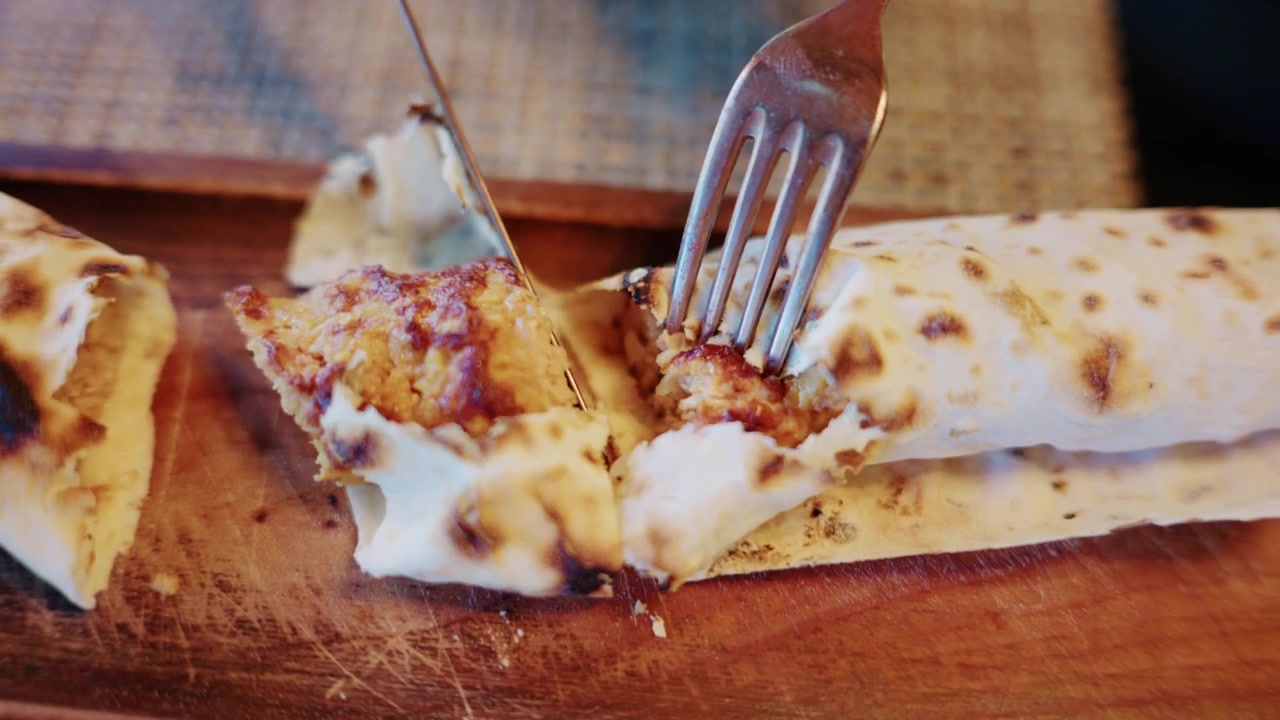 Close up of a stuffed flatbread with lyulya kebab being sliced on a wooden board