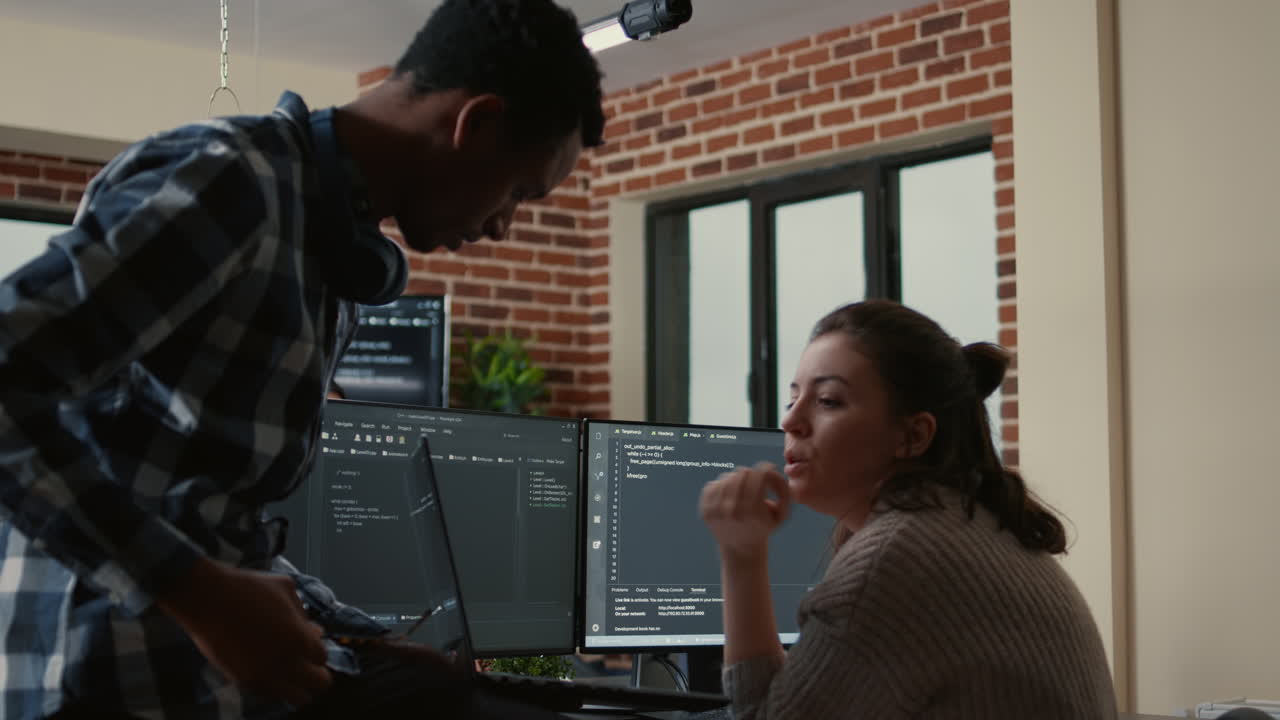 Junior developer sitting down on desk showing laptop with source code to senior dev