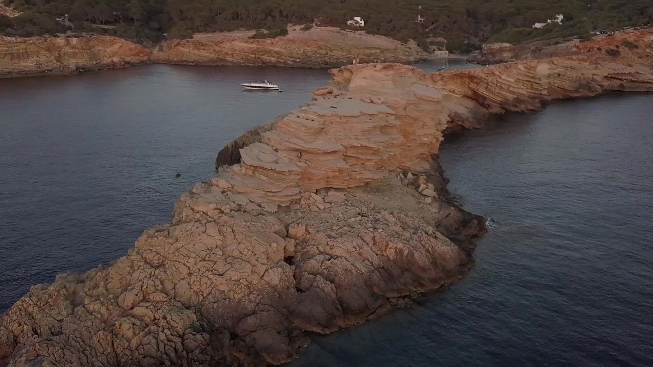 Jævn luftoptagelse i kredsløb af en lille halvø på Ibizas kyst. Billedet viser os klippens særegne former i den gyldne time