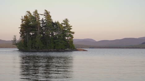 Tight-shot-of-island-on-lake-with-mountains-in-background,-sunset