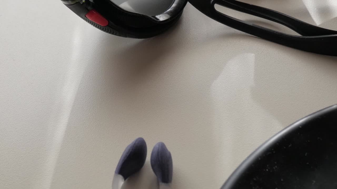 Foto macro de óculos de natação pretos com reflexos em superfície branca sob luz natural suave