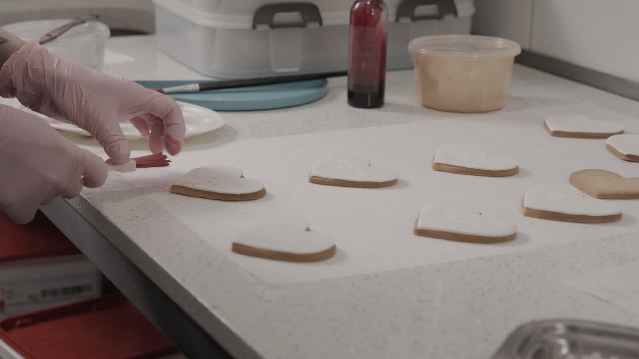 Woman sprays with healthy food coloring frosted butter cookies in the shape of hearts in a pastry shop, 4K