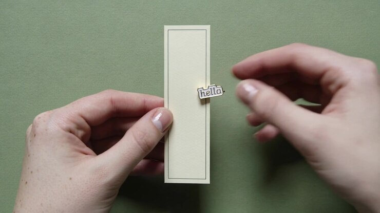 Left hand holding cream card upright, right hand pressing hello sticker onto edge, AI-generated