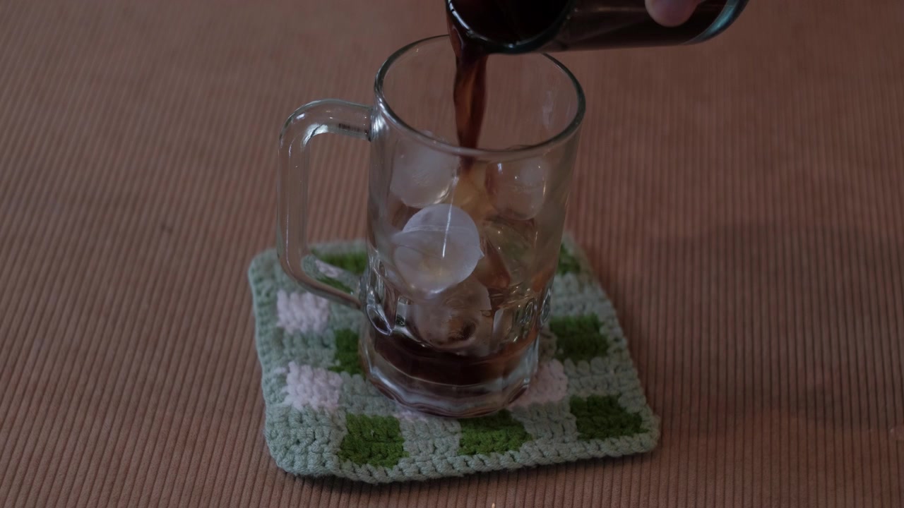 Inquadratura statica di caffè preparato versato in una tazza di vetro con ghiaccio su un tavolo, con una piccola fuoriuscita durante la preparazione casalinga.