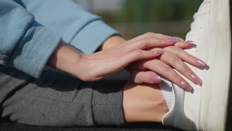 close-up of hands during workout session, with fingers delicately touching foot, showcasing athletic preparation with a focus on nails, athletic shoes, and sports gear in a peaceful environment