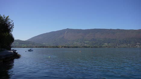 Boat-and-floating-buoys-on-Lake-Annecy-in-the-French-Alps-with-mountain-ridge-in-the-background,-Wide-shot