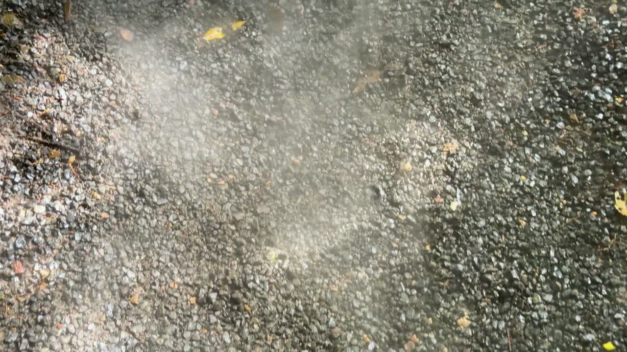 White smoke or vapor drifts across outdoor gravel surface, natural daylight, static camera, close-up