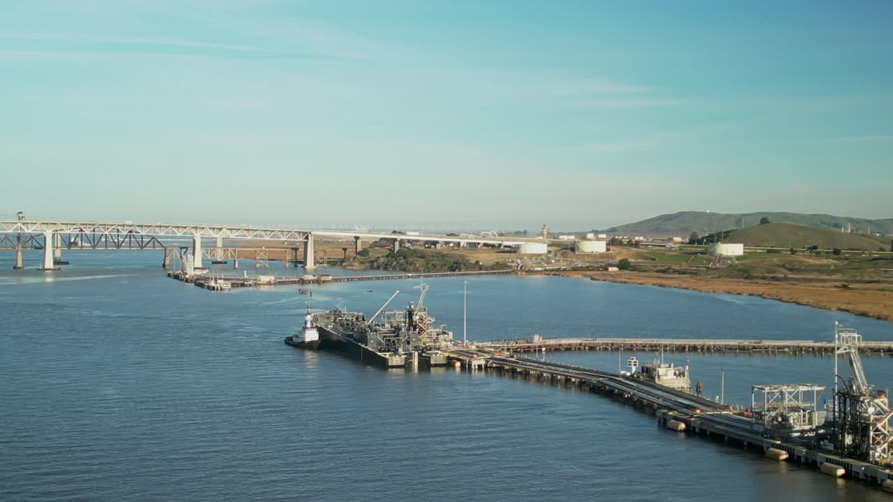 Aerial wide overview of industrial maritime infrastructure and bridges along Carquinez Strait wetlands and shoreline in Martinez, California, with hills
