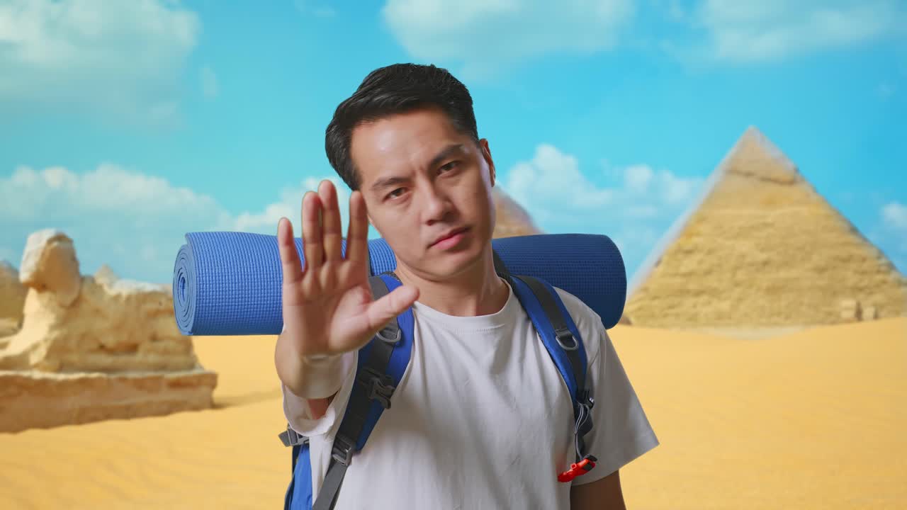 Close Up Of Asian Male Hiker With Mountaineering Backpack Looking At Camera And Making Stop Hand Sign While Traveling In Pyramid Of Giza