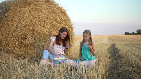 happy family in a wheat field. mother and daughter on a picnic in a wheat field near one of round bales at sunset time