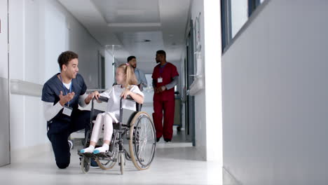 young biracial male nurse assists a caucasian girl in a wheelchair at a hospital