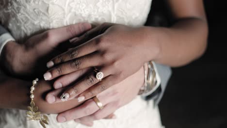 Bride-and-groom-cuddle-with-their-hands-overlapping-and-wedding-bands-showing-while-posing-for-a-photographer-at-night