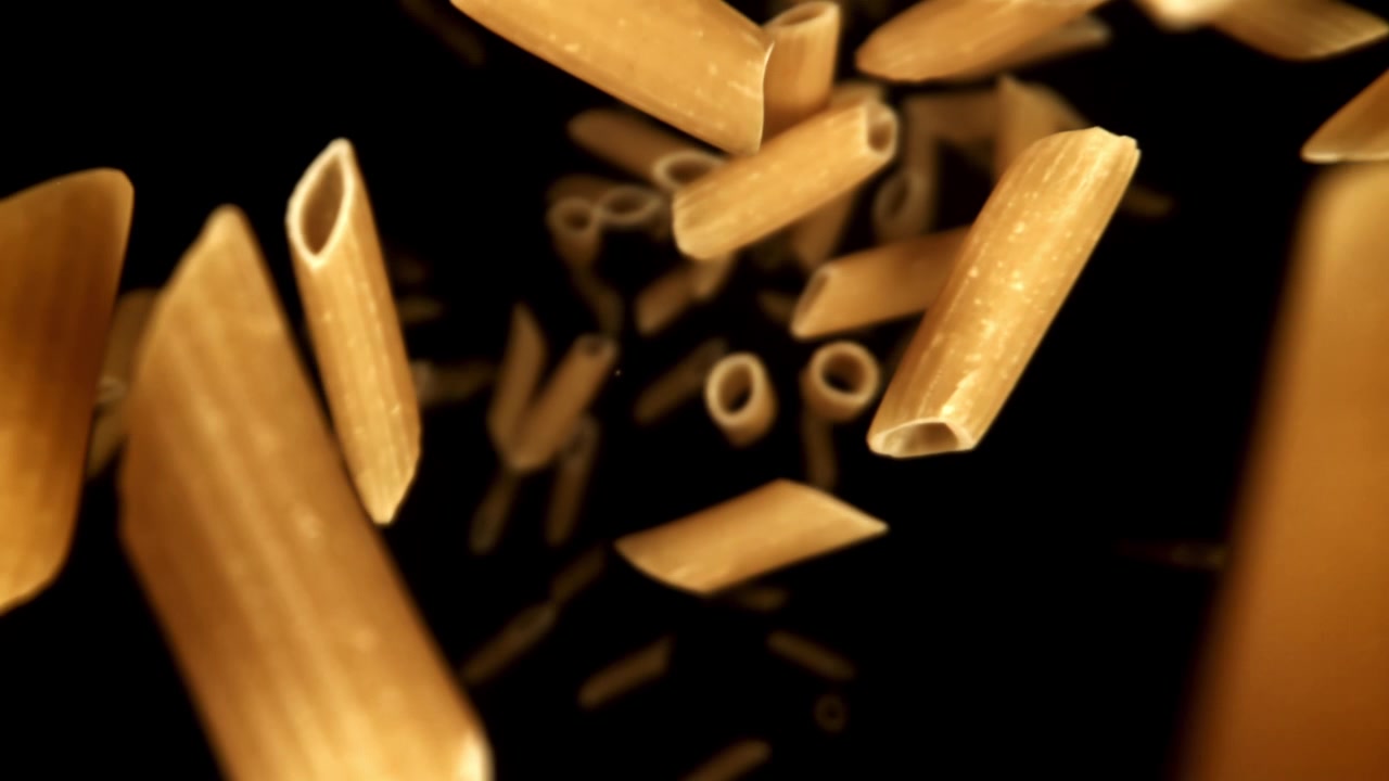 Super rallentatore di pasta penne che cade su sfondo nero.