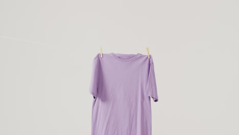 video of close up of purple t shirt hanging on white background