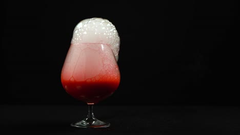 dry ice blood bubbling in a cognac glass with red paint on a black background