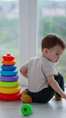 baby boy assembled the colorful toy pyramid. kid wants to take the top but distracts on something and moves back.. vertical video