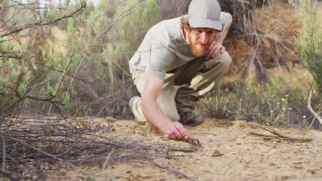 Superviviente-Masculino-Caucásico-En-Cuclillas-Y-Examinando-Animales-Cayendo-En-El-Desierto