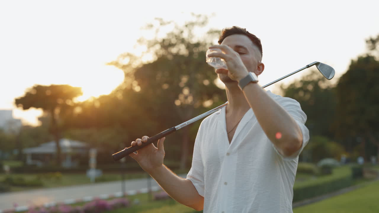 Man Taking a Drink on a Golf Course at Sunset