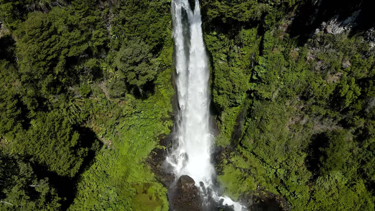 panorámica aérea a la derecha de la cascada salto el león que fluye sobre una piscina rocosa rodeada de un denso bosque verde, pucón, chile