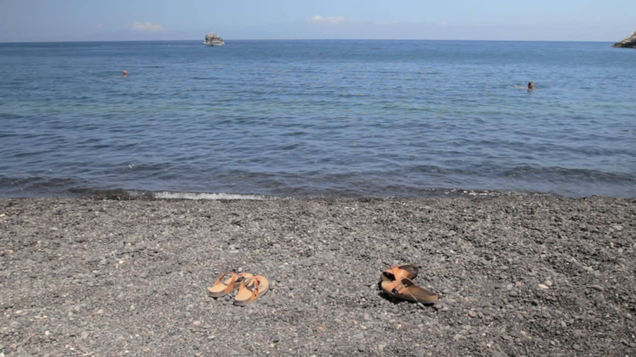 카마리라고 불리는 산토리니의 검은 행상 해변에 가죽 비치 샌들 한 켤레