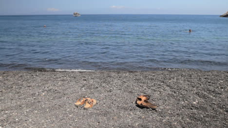 a pair of leather beach sandals on a black peddle beach in santorini, called kamari