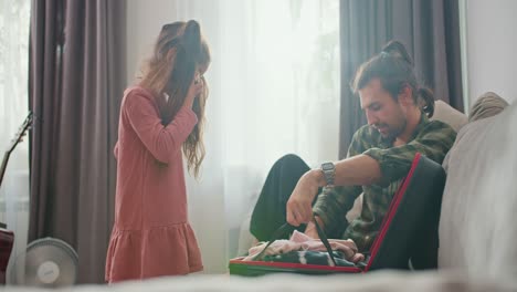 A-little-brunette-girl-in-a-pink-dress-and-her-father,-a-brunette-man-in-a-green-checkered-shirt,-put-their-things-in-a-black-suitcase-and-close-it-before-starting-their-trip