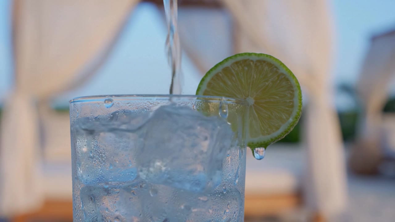 A Refreshing Beverage with Ice and a Lime Slice, Perfectly Set Against a Relaxing Background of Draped Fabric and a Calm Outdoor Atmosphere