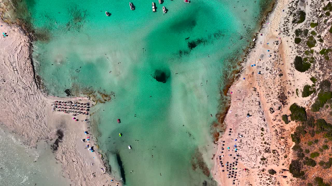 Una splendida vista aerea mostra bellissime acque turchesi che incontrano una spiaggia sabbiosa. Le persone si rilassano e si godono la giornata in riva al mare, mettendo in risalto una vivace scena all'aperto.