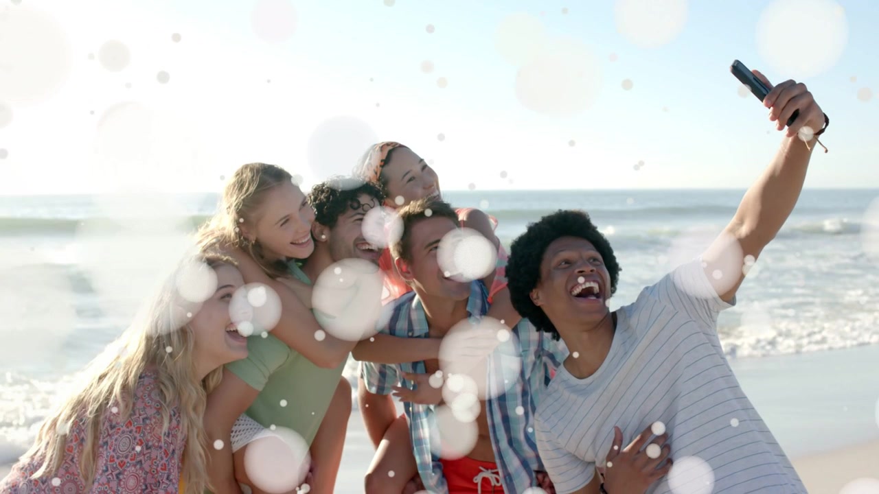 Six friends huddling beach as bokeh overlay fading revealing right raising phone for social selfie