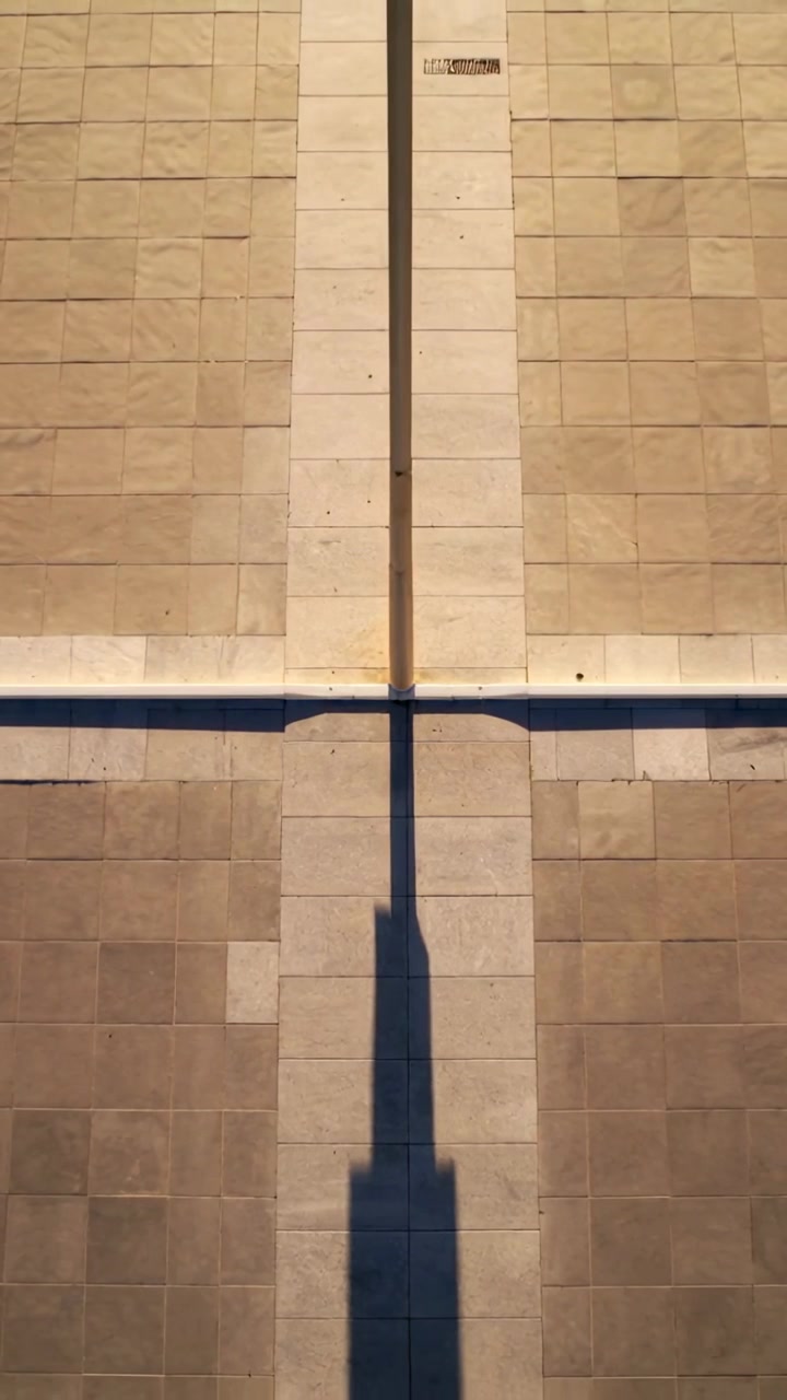 Video verticale: Luce solare che si sposta sfiorando un palo di metallo e l'ombra lungo le piastrelle esterne con fuga.