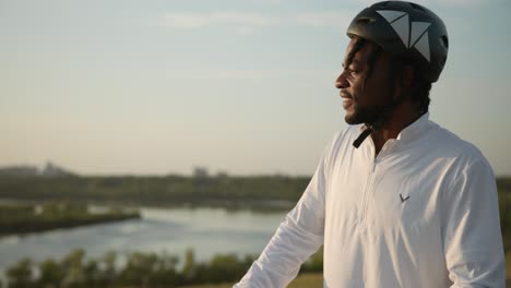 young african-american male looks out to the skyline while sitting on his bike, wearing his helmet