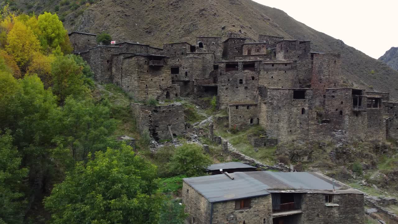 Panning drone fly at ancient Shatili fortress-houses on steep rocky mountain hillside, Khevsureti, Mtskheta-Mtianeti, Georgia
