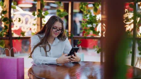 young lady seated at a table using her phone, with glowing decorative lights in the background and other people moving around in a vibrant and dynamic environment