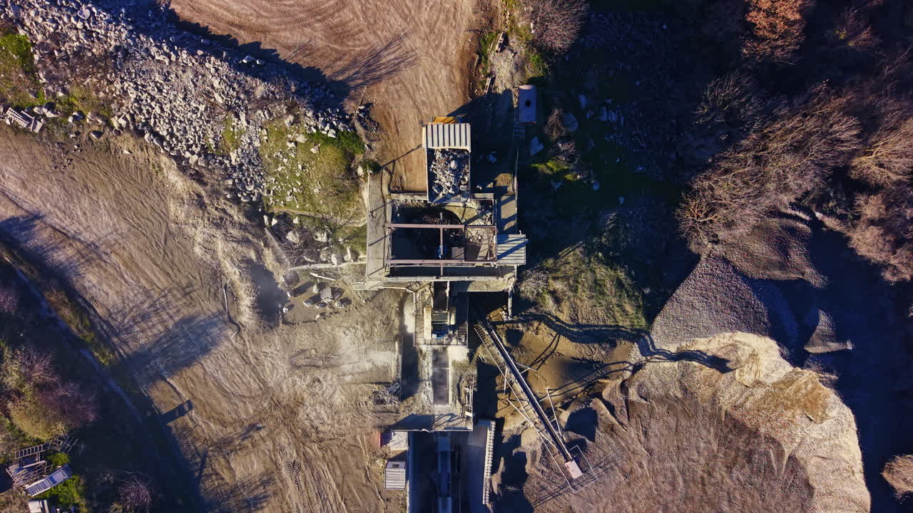 View from above showcases an abandoned quarry with weathered structures surrounded by nature during a bright, clear day