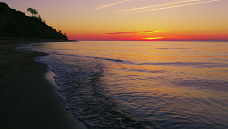 beautiful view of rocky seashore against bright orange sunset in evening.