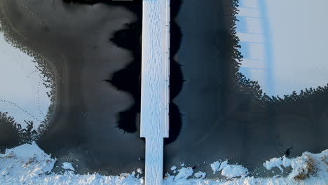 aerial top down shot of of frozen lake with snow-covered jetty footbridge and cracked ice surface