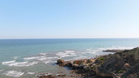 Drone-rises-above-coastline-as-waves-roll-onto-rocky-shoreline-praia-de-santa-eulalia