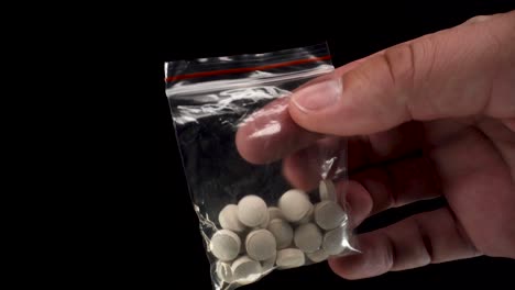 close up view of bitcoin cryptocurrency being used to buy black market drugs, a small transparent bag with grey pills on black background 4k