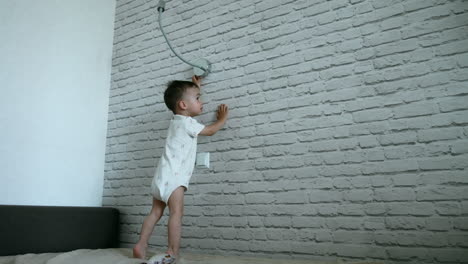 little toddler boy in a romper runs up to a light switch. kid turns on the lamp smiling and jumping cheerfully.