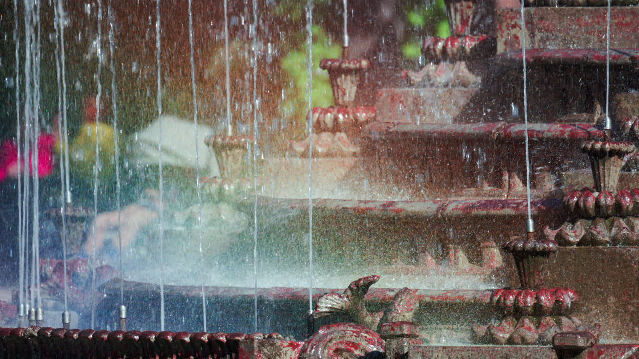 View of a decorative fountain with sparkling water droplets illuminated by sunlight in a park